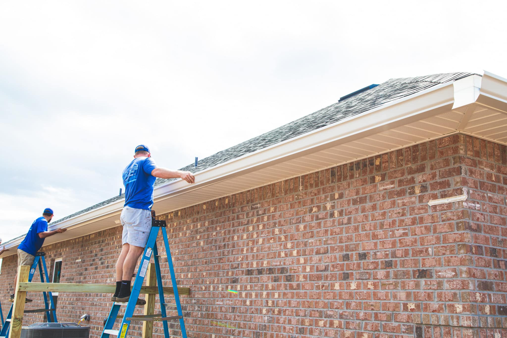 guy in blue shirt installing gutters on a shingle roofing